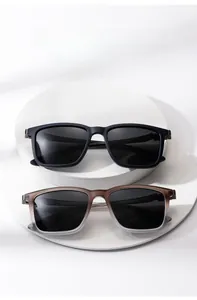 Close-up of modern square sunglasses with matte black and gradient brown frames on white podiums