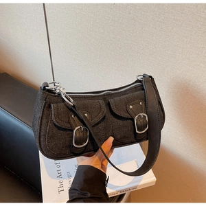 Close-up of black denim shoulder bag featuring twin front pockets and silver buckles