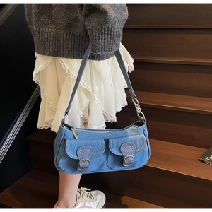 Close-up of blue denim shoulder bag featuring double front flap pockets and silver zipper