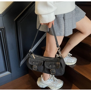 Detail of black denim shoulder bag with dual front pockets and silver buckle accents
