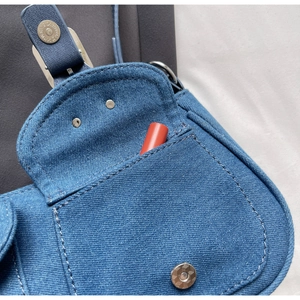 Detail of denim saddle bag with contrast stitching and a lipstick in the front pocket