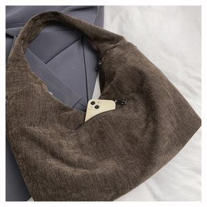 Detail of a brown corduroy shoulder bag showing an outer zipper pocket with a mobile phone