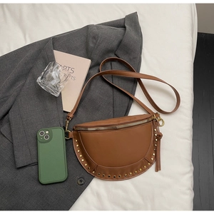 Detailed view of brown leather crescent bag with gold rivets on white fabric background