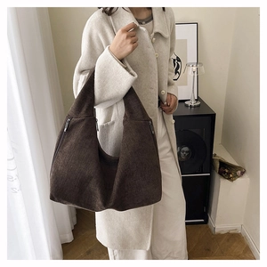 Detail of deep brown canvas tote bag with side metal zipper shown on a beige coat