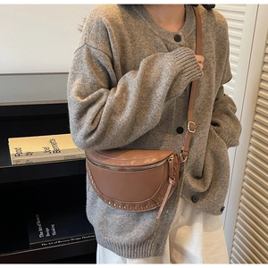 Close-up of caramel brown half-moon crossbody bag with vintage bronze rivets and adjustable strap
