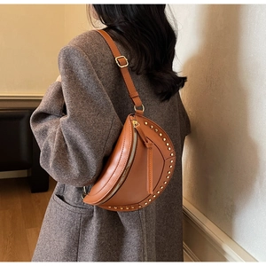 Detail of vintage brown crescent bag with gold rivet accents on a blazer backdrop