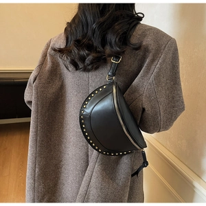 Detail of black leather crescent bag with gold studs worn over a wool coat