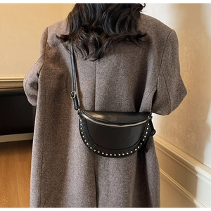 Detail of black crescent crossbody bag with golden studs on textured faux leather surface