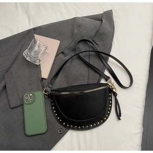 Detail of black crescent crossbody bag with gold studs on a grey suit background