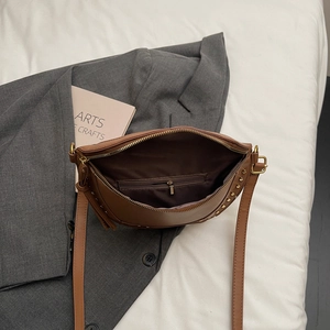 Vintage brown PU leather crossbody bag with gold studs on a grey blazer backdrop