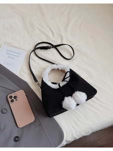 Detailed shot of black faux suede crossbody bag with white plush trim and fuzzy pom-poms