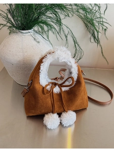 Detail of plush lamb wool trim and decorative pom-poms on the brown suede dumpling bag