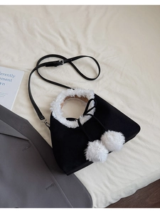 Close-up of black faux suede triangular bag with white plush fur trim and soft pom-poms