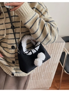 Detail of black crossbody bag with white faux fur trim and two plush decorative pom-poms