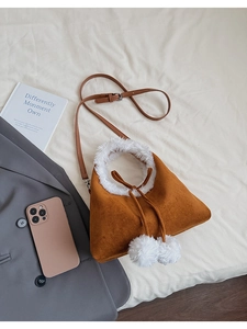 Brown suede faux fur crossbody bag with white pom-pom drawstrings and leather strap