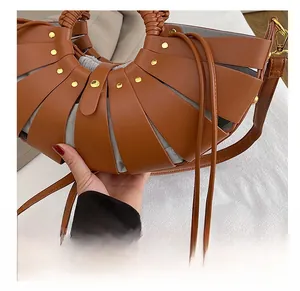 Detail of hollow brown leather shell handbag with gold rivets and grey drawstring pouch