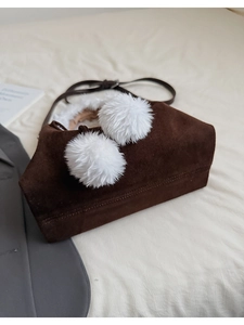 Detail of brown suede crossbody bag with large white faux fur pom-pom decorations