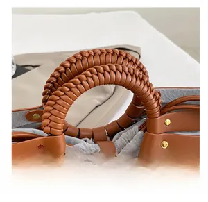 Detailed close-up of brown leather handbag featuring woven handle and gold rivet accents