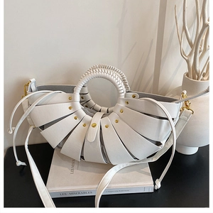 Close-up of white woven basket bag with gold studs and circular braided handle detail