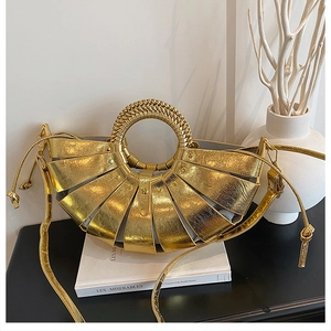 Close-up of golden woven fan-shaped handbag with textured metallic finish on a book
