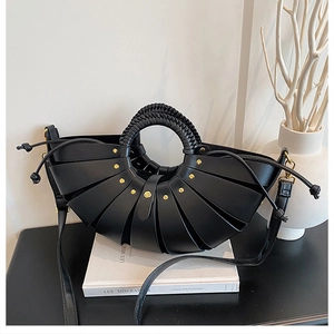Detail of black woven handle handbag with shell pleats and gold studs on a book