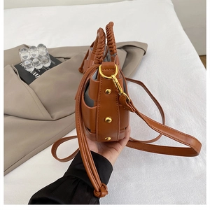 Close-up of caramel leather handbag featuring braided handles and golden rivet details