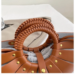 Macro detail of brown leather handbag with braided handle, gold studs and drawstring liner