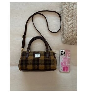 Top view of a Boston style plaid handbag with leather straps on a beige fabric background