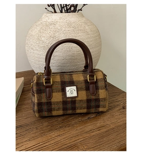 Detail shot of brown plaid wool Boston bag with leather handles on a wooden table