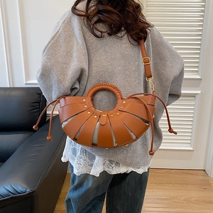 Brown woven leather bucket bag with top handle and adjustable shoulder strap worn by model