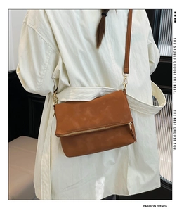 Close-up of brown textured leather crossbody bag with decorative gold metal zipper detail