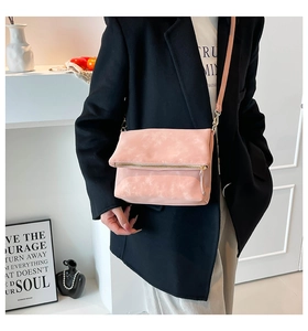 Detail of pink suede crossbody bag with gold zipper and thin shoulder strap worn by model