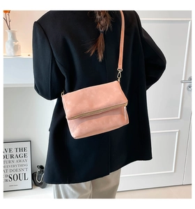 Detail of pink faux leather crossbody bag with gold zipper on a black coat back view