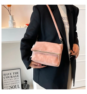 Detailed view of pink crossbody bag with matte finish and gold zipper on a black blazer