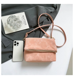 Detail of powder pink saddle bag with golden zipper and slim strap beside a smartphone