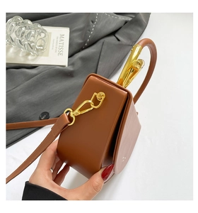 Detailed side view of brown leather handbag with gold metal handle and long shoulder strap