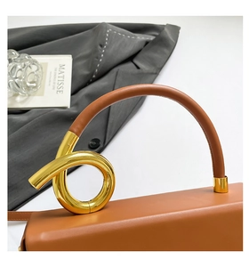 Detail of a brown leather handbag featuring a unique gold metal ring knot handle design