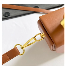 Detailed macro view of caramel leather handbag strap with golden metal lobster clasp and stitching
