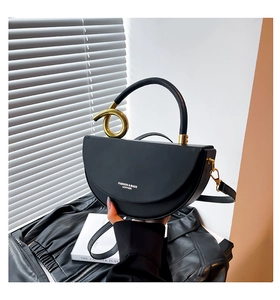 Detail of black leather half-moon bag with golden twist metal rings and detachable strap