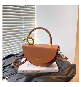 Detailed macro view of a brown leather saddle bag featuring gold metal knot accents