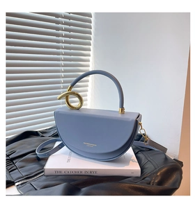 Detail of light blue box bag with a golden twisted ring handle on a white book