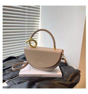 Detailed macro of a beige saddle bag with a unique gold twisted metal handle accessory
