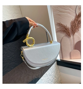 Close-up of silver crescent handbag with golden metal ring and leather strap details