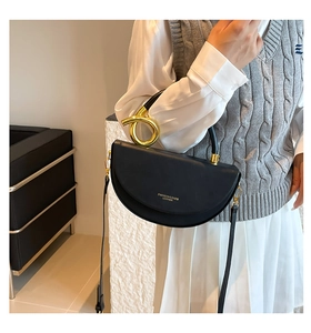 Detail of a black leather saddle bag with gold metal handle on a model's shoulder