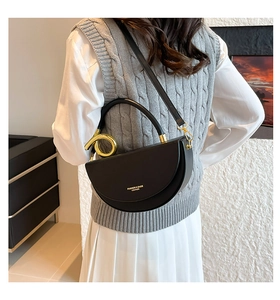 Detail of black leather saddle bag featuring a unique gold metal ring handle and strap
