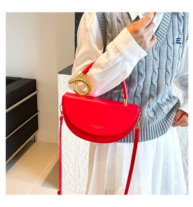 Detail of red leather saddle bag featuring a bold gold circular metal handle and smooth finish