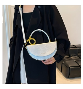 Detail of silver crescent leather handbag with gold ring handle worn on a black coat