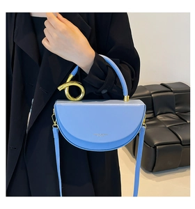 Close-up of light blue leather saddle bag with gold metal ring handle and logo detail