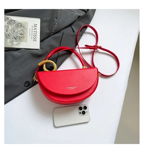 Detail view of red semi-circle saddle bag with gold metal handle on a minimalist setup