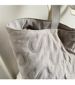 Macro shot of grey quilted tote bag with S-shaped stitching and JL logo tag detail